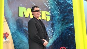 Author Steve Alten Wearing Sunglasses and a Black Suit Standing on the Red Carpet at the Premiere of 'The Meg' in Front of a Large Poster of a Shark About to Erupt Out of the Ocean