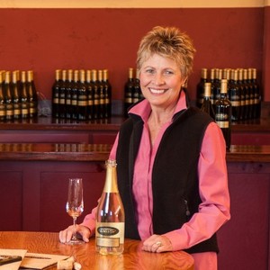 Woman who is the founder of a winery stands smiling with glass of sparkling wine