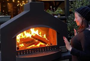 A woman has her hands up as she feels the warmth from the fire in an Bakewell Burner outdoor fireplace oven.