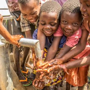 Children from Ugandan village play in water at new water well drilled in rural Uganda